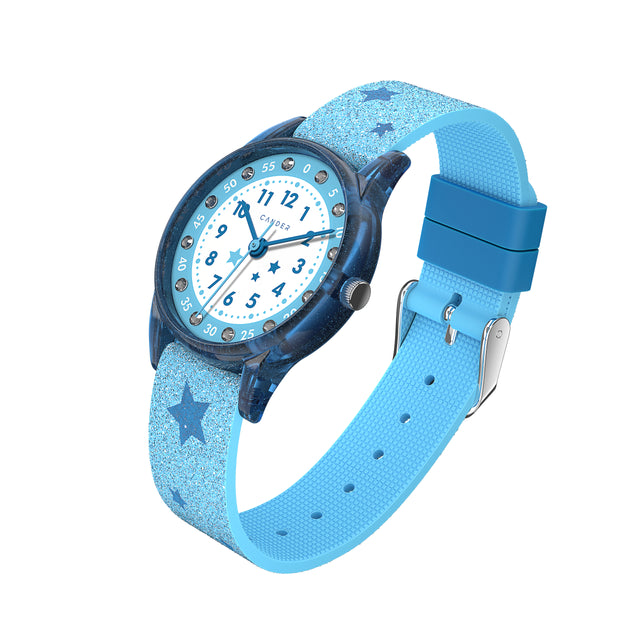 Eine Kinder-Armbanduhr mit einem hellblauen Glitzerarmband, auf dem dunkelblaue Sternchen abgebildet sind, blau-transparentem Gehäuse mit eingearbeitetem Glitzer und kleinen Schmucksteinen auf dem Ziffernblatt. Die Zahlen auf dem blau- weißem Ziffernblatt sind sehr gut ablesbar.