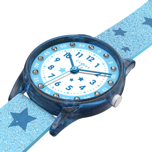 Eine Kinder-Armbanduhr mit einem hellblauen Glitzerarmband, auf dem dunkelblaue Sternchen abgebildet sind, blau-transparentem Gehäuse mit eingearbeitetem Glitzer und kleinen Schmucksteinen auf dem Ziffernblatt. Die Zahlen auf dem blau- weißem Ziffernblatt sind sehr gut ablesbar.