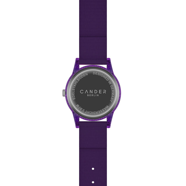 Eine Kinder-Armbanduhr mit einem lila Stoffarmband, auf dem kleine Sterne abgebildet sind. Das lila-transparente Gehäuse hat ein Glitzereffekt. Auf dem Ziffernblatt befinden sich kleine Schmucksteine. Die weißen Zahlen auf dem lila Ziffernblatt sind sehr gut ablesbar.